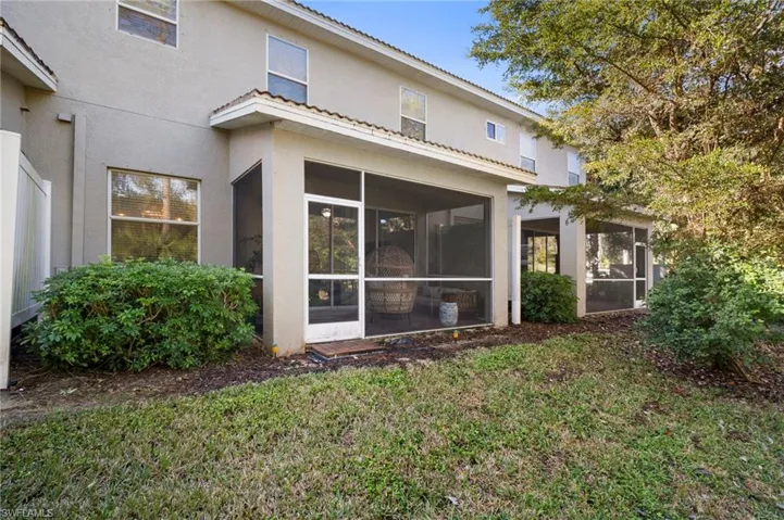 Rear view of property with stucco siding, a tile roof, a yard, and a sunroom