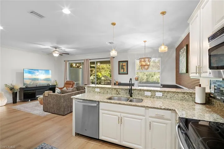 Kitchen featuring a peninsula, white cabinets, appliances with stainless steel finishes, hanging light fixtures, and light stone counters