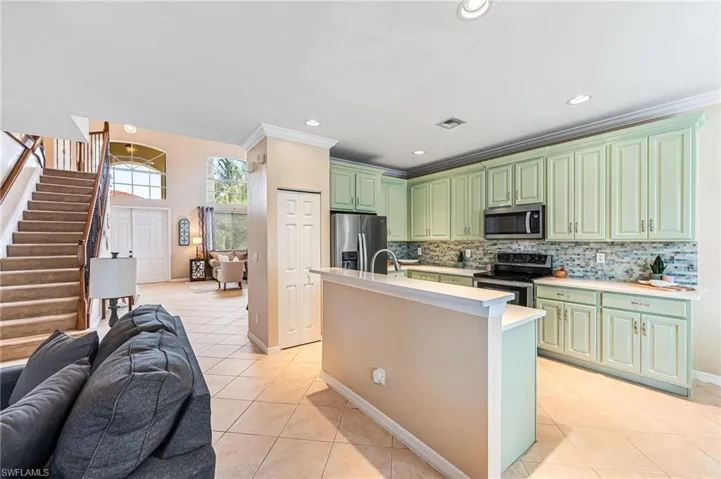 Kitchen featuring decorative backsplash, green cabinetry, light tile patterned floors, an island with sink, and stainless steel appliances