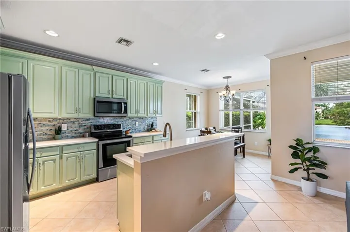 Kitchen featuring stainless steel appliances, pendant lighting, decorative backsplash, green cabinetry, and light tile patterned flooring