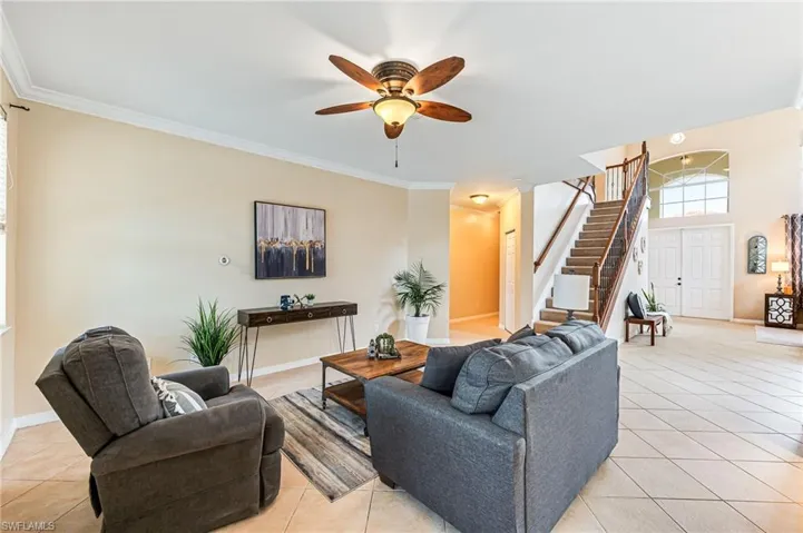 Living room with ceiling fan, crown molding, and light tile patterned floors