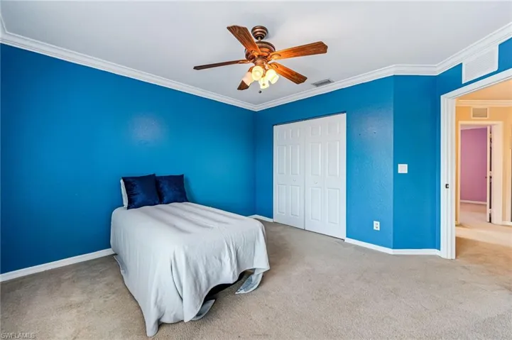 Carpeted bedroom with ceiling fan, ornamental molding, and a closet