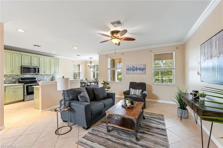 Living room featuring ceiling fan with notable chandelier, light tile patterned floors, and crown molding