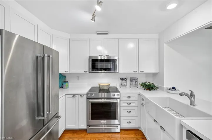 Kitchen with appliances with stainless steel finishes, light countertops, white cabinetry, and wood floors