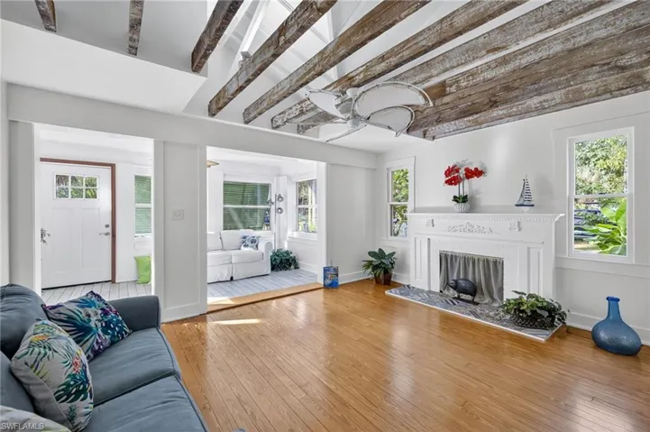 Living room with a fireplace with raised hearth, hardwood  flooring, healthy amount of natural light, and beam ceiling