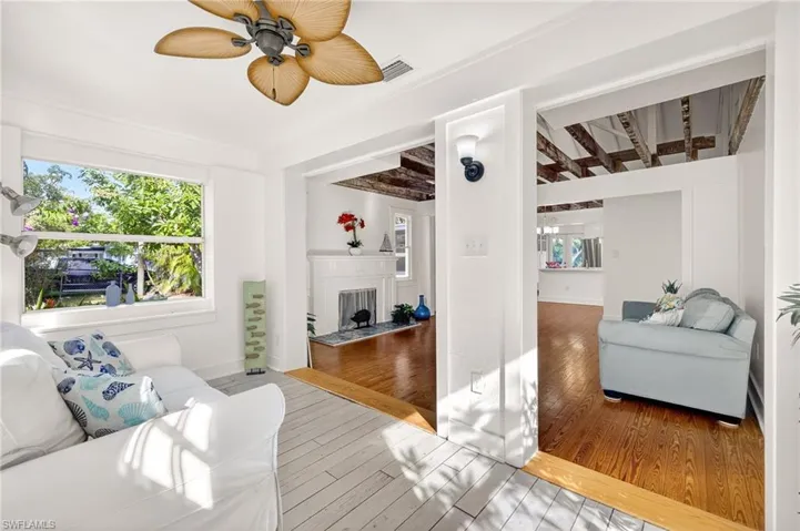 Living room featuring wood flooring, ceiling fan, a fireplace, and beamed ceiling