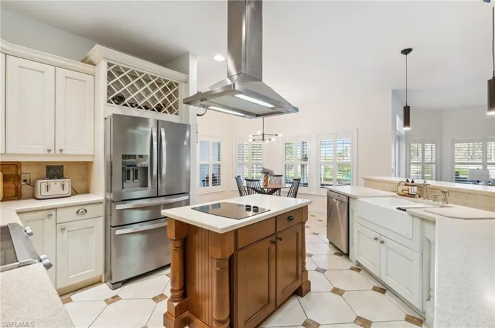 Kitchen featuring a healthy amount of sunlight, island exhaust hood, stainless steel appliances, and decorative light fixtures