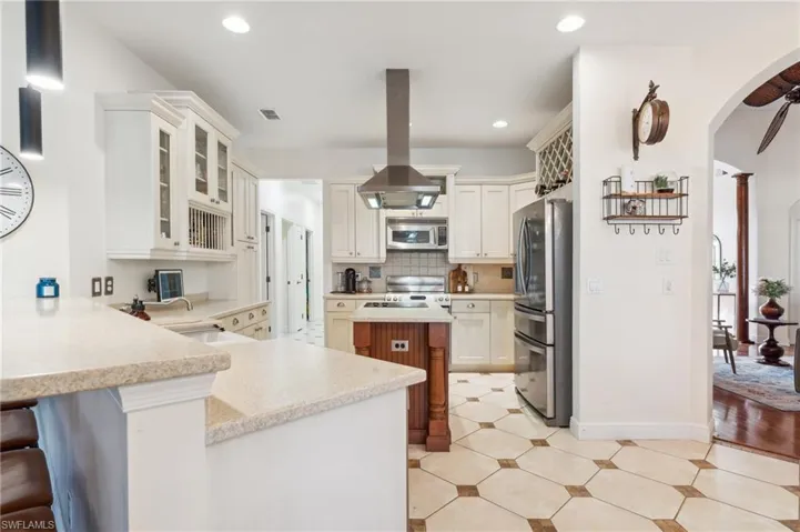 Kitchen with island range hood, a breakfast bar area, kitchen peninsula, stainless steel appliances, and sink