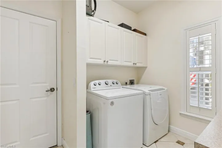 Clothes washing area featuring independent washer and dryer, light tile patterned floors, and cabinets