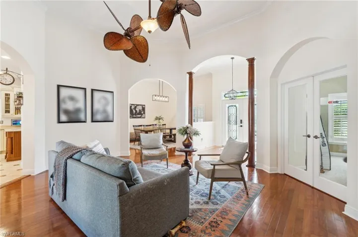 Living room featuring a towering ceiling, decorative columns, ceiling fan, dark wood-type flooring, and ornamental molding