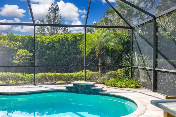 Screened pool area featuring a curved swimming pool with water feature, tile surrounding paver deck, complete private rear yard