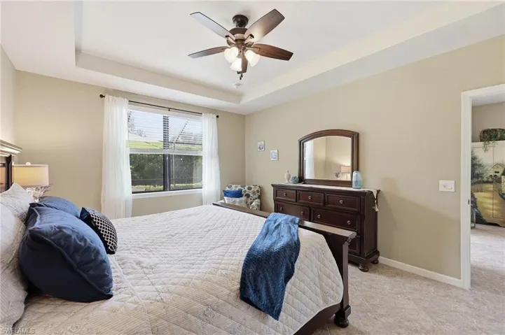Bedroom featuring a tray ceiling, ceiling fan with integrated lighting, window with blinds, and tile flooring