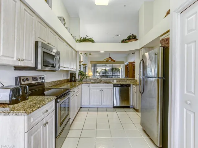 Kitchen featuring stainless steel appliances, dark stone countertops, light tile patterned floors, a towering ceiling, and white cabinetry