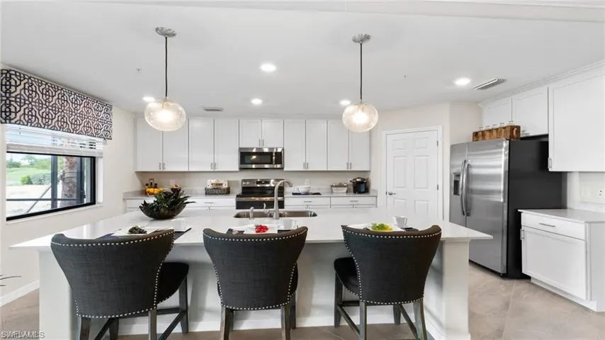 Kitchen with appliances with stainless steel finishes, a sink, light countertops, white cabinets, and a kitchen bar