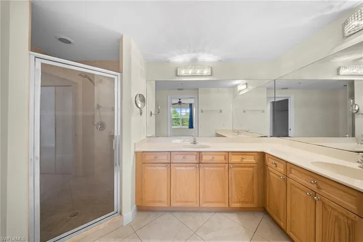 Spacious bathroom featuring a glass-enclosed shower, extensive vanity with dual integrated sinks, light wood cabinetry, large wall-mounted mirrors, and tiled flooring