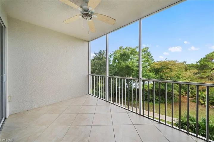 Screened balcony featuring textured wall finishes, tile flooring, a ceiling fan, and metal railings overlooking mature trees and vegetation