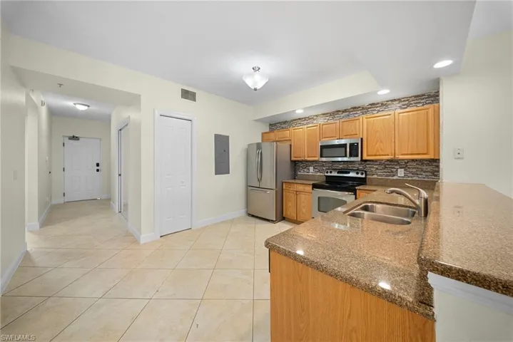 Kitchen featuring stainless steel appliances, wood-finish cabinetry, a textured backsplash, and stone-finish countertops