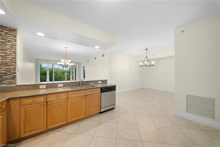 Kitchen area featuring wood cabinetry, granite-style countertops, stainless steel dishwasher, and tile flooring