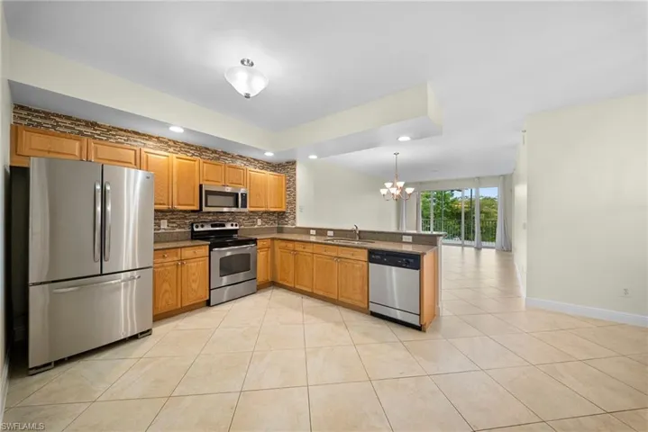 Kitchen featuring stainless steel appliances, wood cabinetry, stone-look countertops, and a full-height tile backsplash