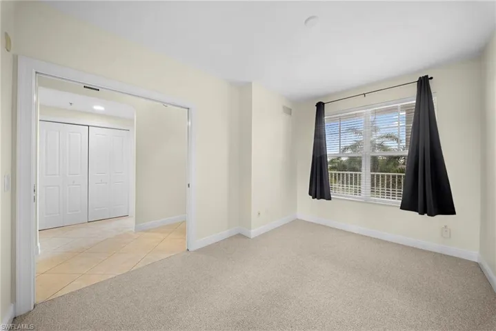 Spacious room featuring neutral carpeting, a large window with white blinds, and light cream-colored walls