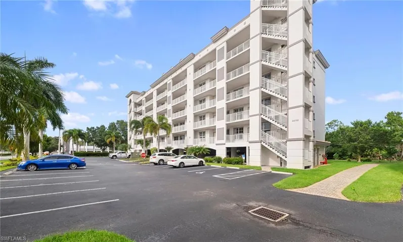 Multi-story residential building featuring white exterior siding, numerous private balconies with white railings, and an exterior stairwell