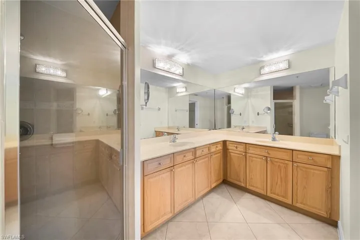 Bathroom featuring a corner vanity with dual sinks, light wood cabinetry, and a large mirror