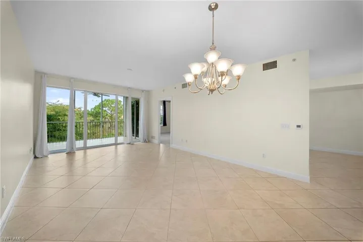 Open living area featuring large format diagonal tile flooring, a multi-light chandelier, and full-height sliding glass doors opening to a balcony with tree-lined scenery