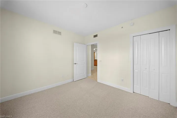 Carpeted room featuring a white bi-fold closet, a single paneled door with brushed nickel hardware, and light-toned walls