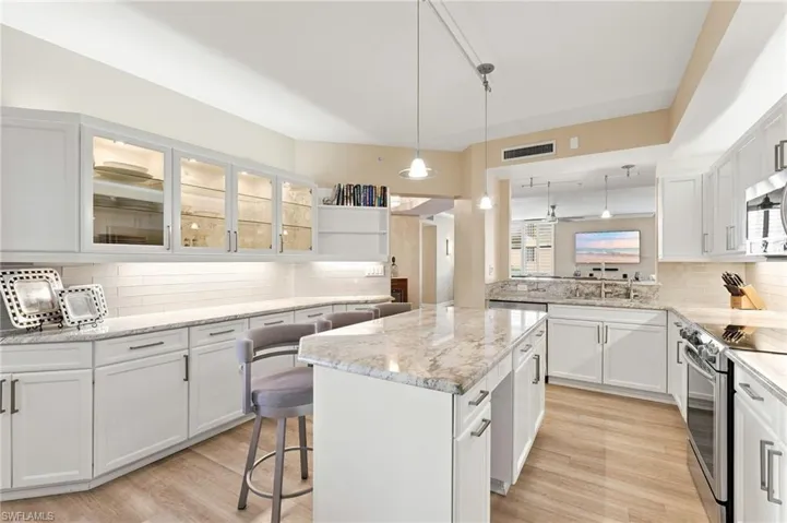 The reimagined kitchen showcases beautiful granite countertops, a custom-designed island, abundant cabinetry, elegant buffet-style serving cabinetry, under and above cabinet lighting, an exquisite backsplash, and sleek stainless-steel appliances. Glass-front cabinetry adds both sophisticated style and valuable additional storage, making this kitchen as functional as it is beautiful.