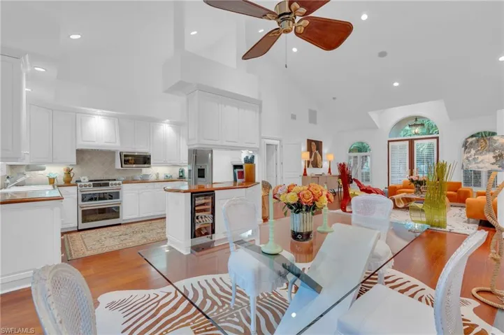 Dining area featuring beverage cooler, ceiling fan, sink, high vaulted ceiling, and light hardwood / wood-style flooring
