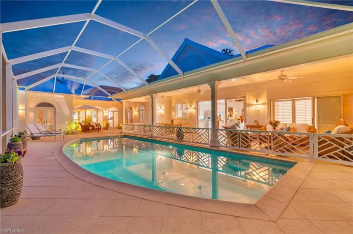 Pool at dusk featuring glass enclosure, french doors, ceiling fan, and a patio