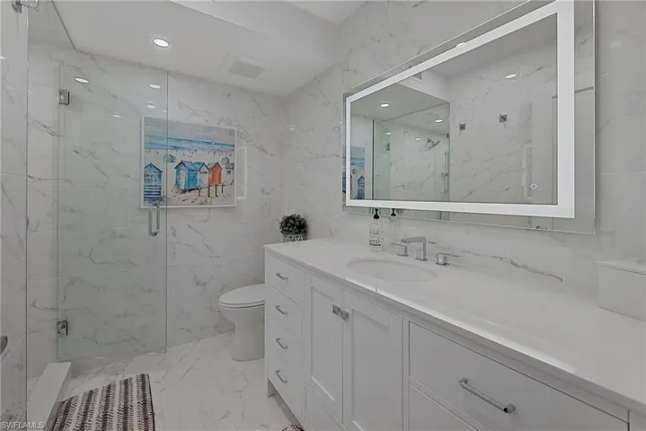 Full bath with light marble finish floors, tile walls, a marble finish shower, vanity, and stone wall