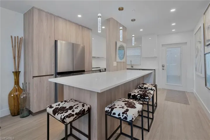 Kitchen featuring hanging light fixtures, modern cabinets, light stone countertops, light wood-style floors, and a center island