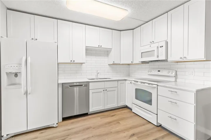 Kitchen featuring sink, tasteful backsplash, light hardwood / wood-style flooring, white appliances, and white cabinets