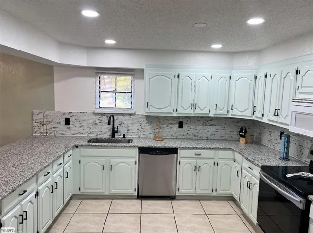 Kitchen with light tile patterned floors, a sink, appliances with stainless steel finishes, and light stone countertops