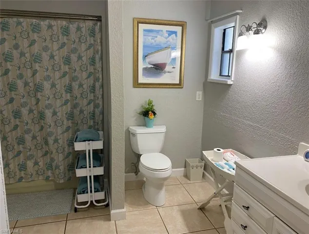 Full bathroom featuring a shower with curtain, tile patterned floors, toilet, and a textured wall