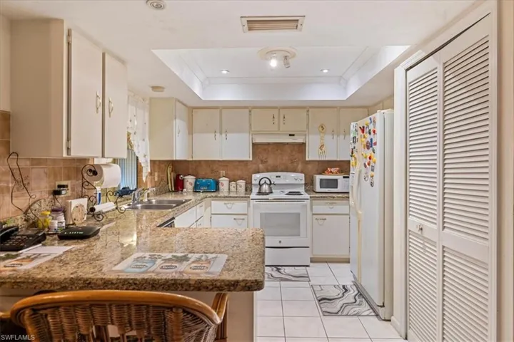 Kitchen featuring white appliances, light tile patterned flooring, a raised ceiling, and kitchen peninsula