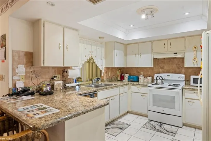 Kitchen featuring white appliances, light stone counters, kitchen peninsula, and a tray ceiling