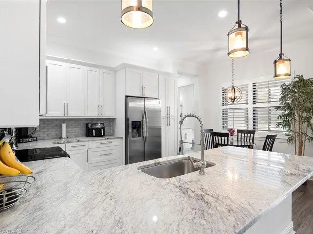 Kitchen with stainless steel refrigerator with ice dispenser, a sink, light stone counters, tasteful backsplash, and pendant lighting
