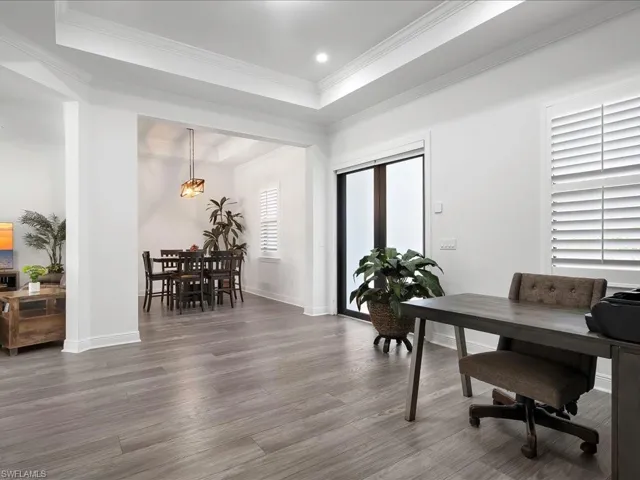 Office area featuring wood finished floors, a raised ceiling, baseboards, ornamental molding, and recessed lighting