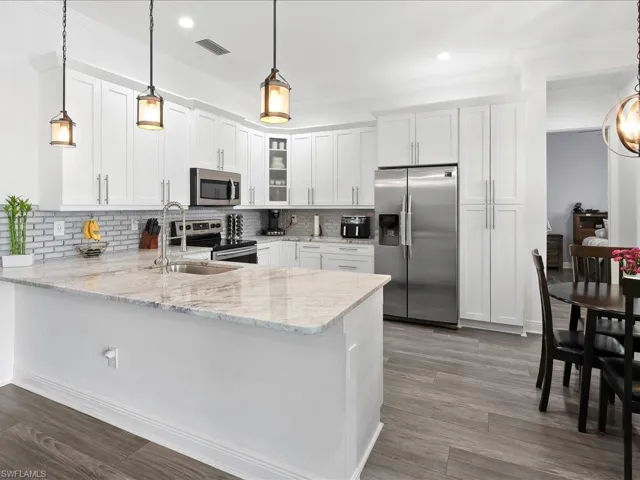 Kitchen with appliances with stainless steel finishes, a peninsula, a sink, glass insert cabinets, and decorative backsplash