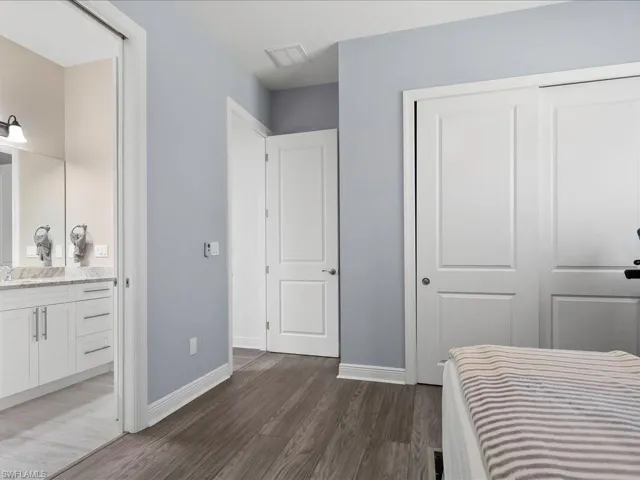 Bedroom featuring dark wood-type flooring, baseboards, a closet, a sink, and ensuite bathroom