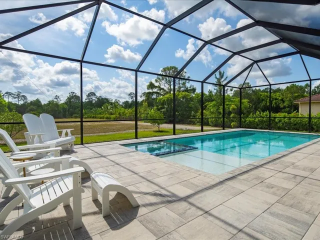 View of swimming pool with a patio, view of wooded area, a pool with connected hot tub, and glass enclosure