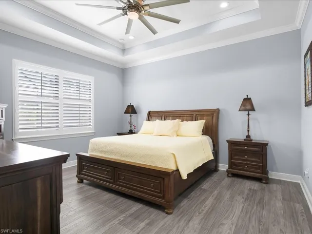 Bedroom featuring a raised ceiling, wood finished floors, baseboards, recessed lighting, and crown molding