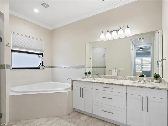 Full bath featuring double vanity, a stall shower, a bath, ornamental molding, and ensuite bathroom