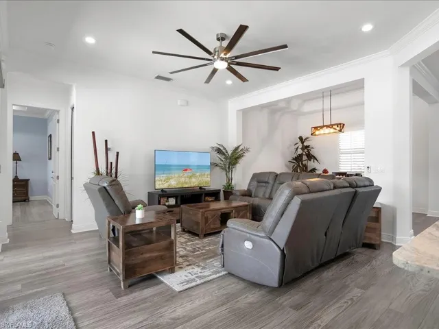 Living area with ceiling fan, wood finished floors, ornamental molding, baseboards, and a chandelier
