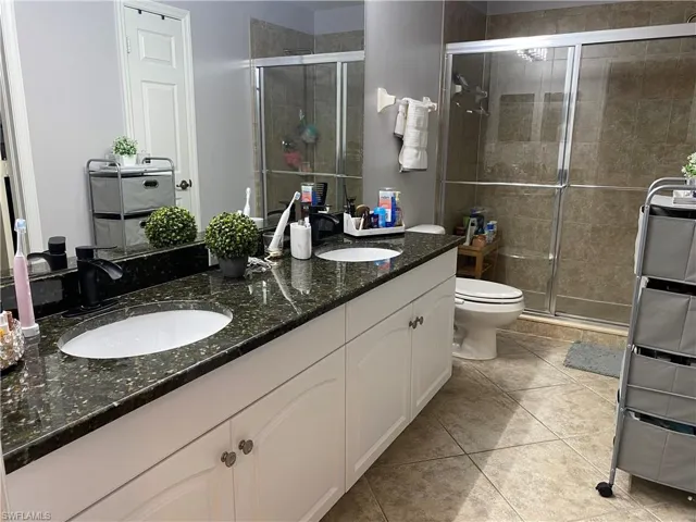 MasterBathroom featuring a shower with shower door, dual bowl vanity, toilet, and tile patterned flooring