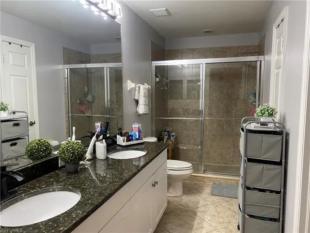 MasterBathroom featuring toilet, double vanity, walk in shower, and tile patterned flooring