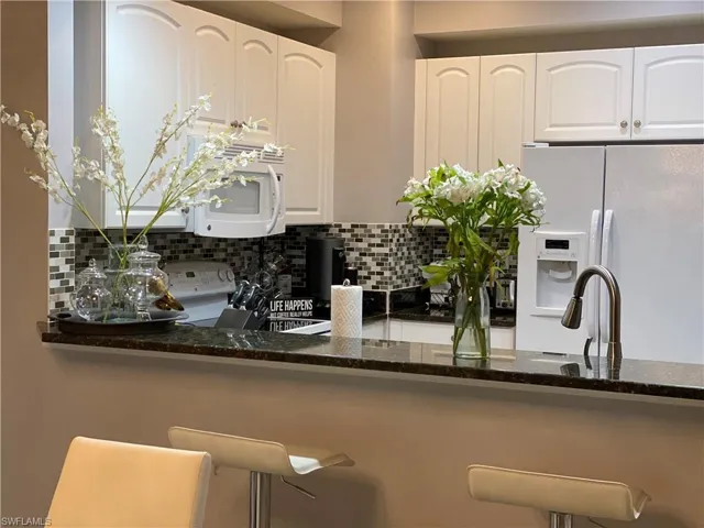 Kitchen with tasteful backsplash, white appliances, white cabinetry, dark stone counters, and sink