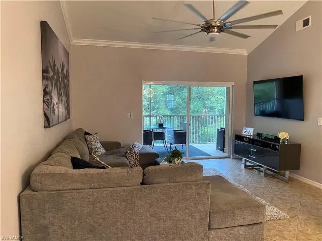 Living room featuring vaulted ceiling, light tile patterned floors, crown molding, and ceiling fan